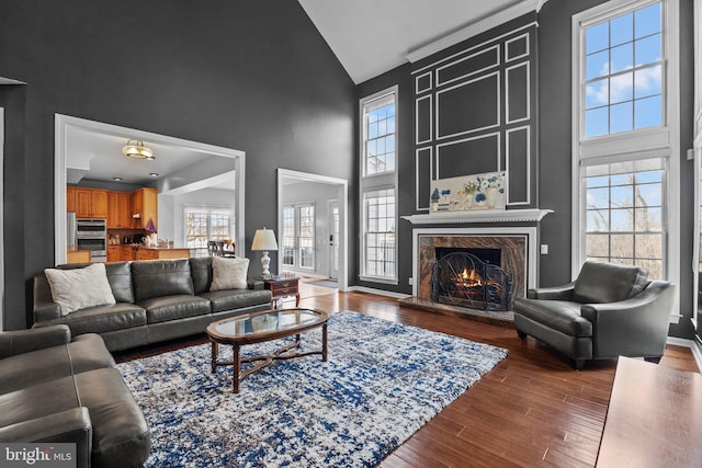 living room with a wealth of natural light, a premium fireplace, high vaulted ceiling, and wood finished floors