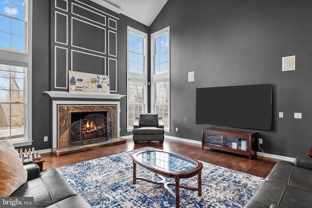 living area featuring a premium fireplace, baseboards, high vaulted ceiling, and wood finished floors