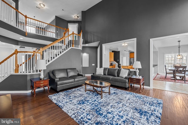 living room with a towering ceiling, stairs, baseboards, and wood-type flooring