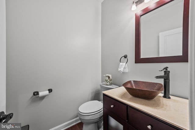 half bathroom featuring toilet, vanity, and baseboards