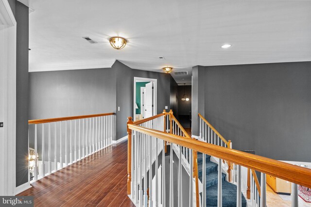 hall featuring visible vents, an upstairs landing, baseboards, and wood finished floors