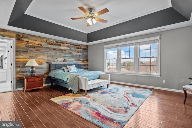 bedroom with visible vents, a tray ceiling, wood finished floors, baseboards, and an accent wall