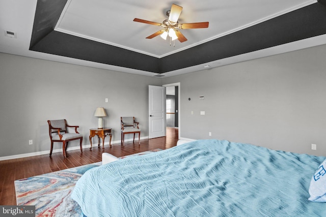 bedroom featuring ceiling fan, a tray ceiling, baseboards, and wood finished floors