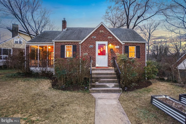 bungalow-style house featuring a shingled roof, brick siding, a yard, and a chimney