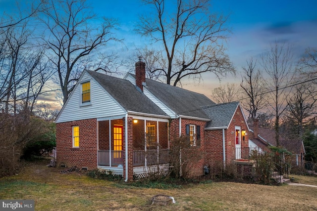 view of front of home with brick siding, a shingled roof, a chimney, a porch, and a front yard