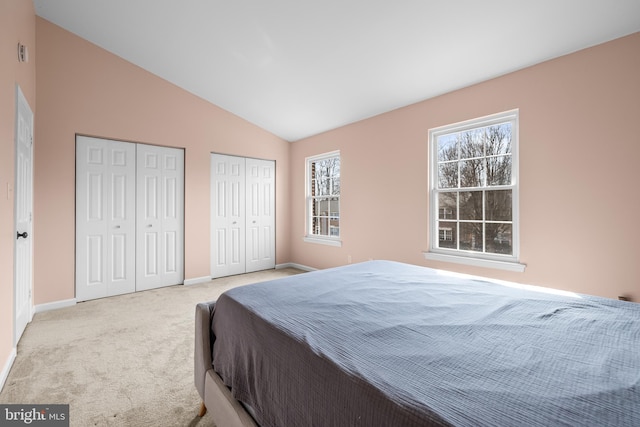 bedroom with lofted ceiling, light colored carpet, and two closets