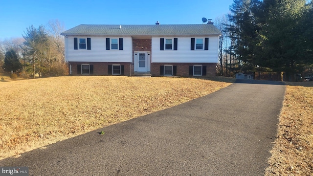 raised ranch featuring driveway, brick siding, a front yard, and entry steps