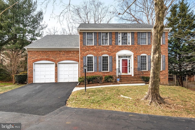 colonial home with aphalt driveway, brick siding, roof with shingles, an attached garage, and a front lawn