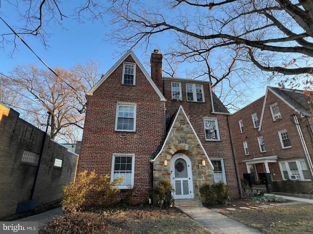 tudor home with brick siding, stone siding, and a chimney