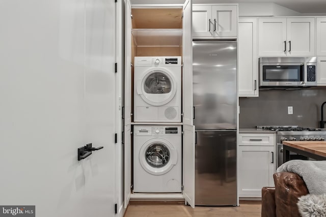 clothes washing area with laundry area, light wood-style flooring, and stacked washer and clothes dryer