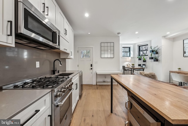 kitchen with white cabinets, light wood-style flooring, appliances with stainless steel finishes, wooden counters, and a sink