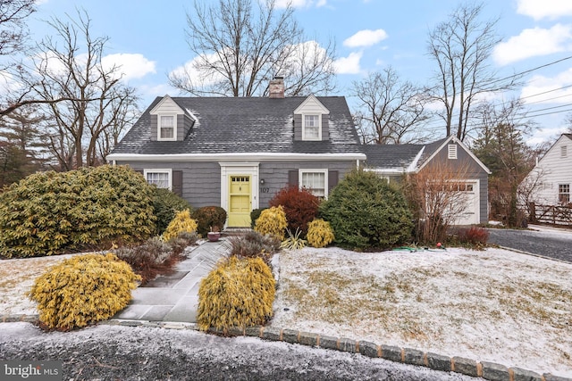 cape cod house featuring aphalt driveway, a chimney, an attached garage, and a shingled roof