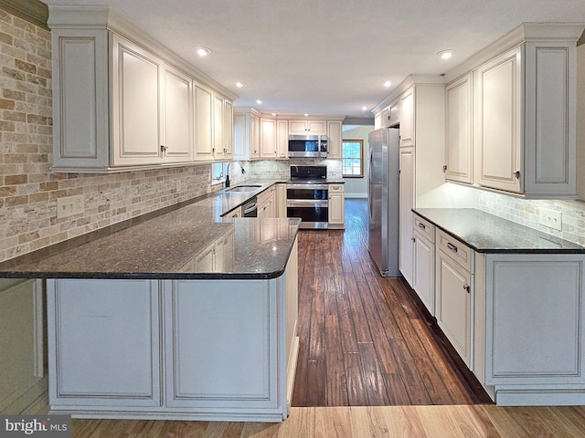 kitchen featuring appliances with stainless steel finishes, dark wood-type flooring, kitchen peninsula, sink, and dark stone countertops