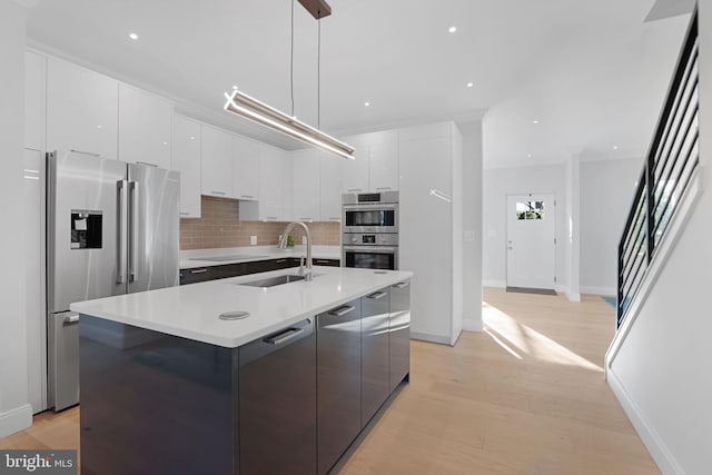 kitchen featuring a center island with sink, white cabinets, hanging light fixtures, stainless steel appliances, and a sink