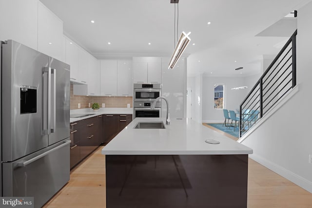 kitchen with stainless steel appliances, light countertops, an island with sink, and dark brown cabinets