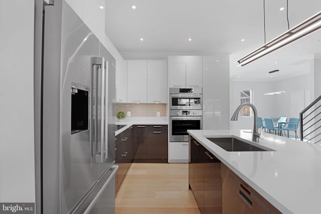 kitchen featuring appliances with stainless steel finishes, white cabinets, light countertops, and a sink