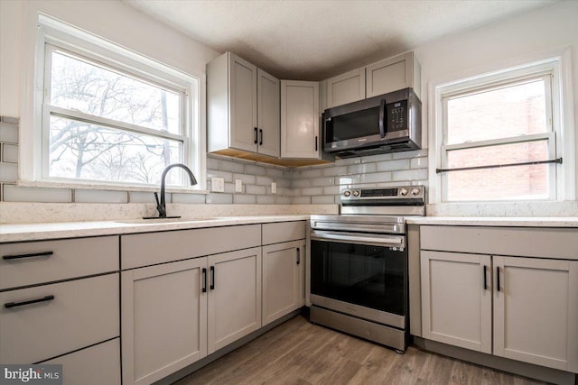 kitchen featuring tasteful backsplash, gray cabinetry, stainless steel appliances, light hardwood / wood-style floors, and sink