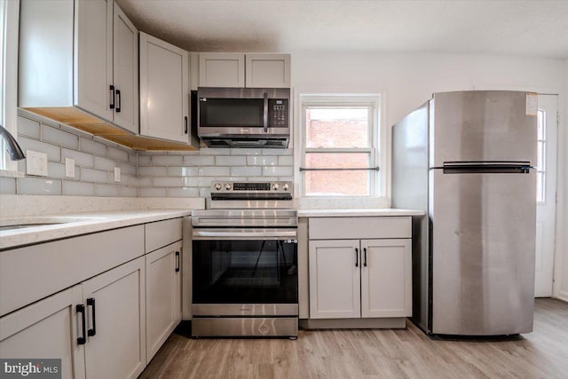 kitchen featuring appliances with stainless steel finishes, sink, a textured ceiling, light hardwood / wood-style floors, and tasteful backsplash