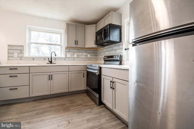 kitchen featuring light wood-type flooring, sink, tasteful backsplash, a textured ceiling, and appliances with stainless steel finishes