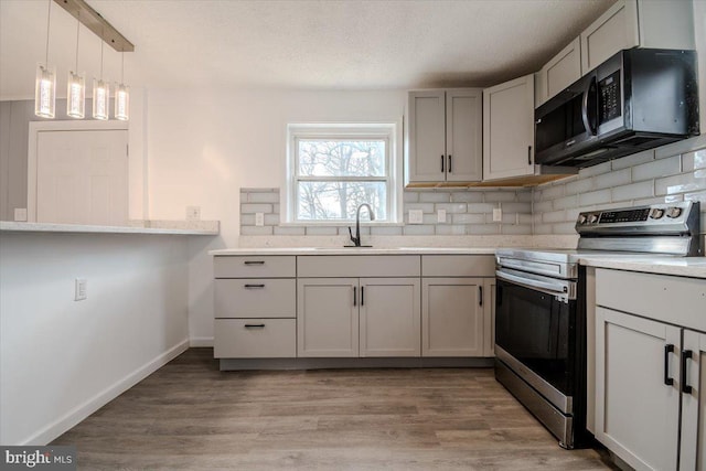 kitchen with tasteful backsplash, stainless steel range with electric stovetop, decorative light fixtures, light hardwood / wood-style floors, and sink