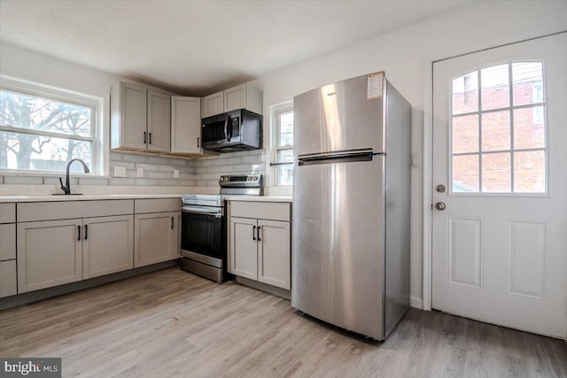 kitchen with tasteful backsplash, gray cabinetry, stainless steel appliances, light hardwood / wood-style floors, and sink