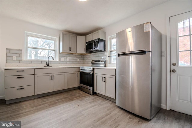 kitchen with appliances with stainless steel finishes, sink, light hardwood / wood-style flooring, and tasteful backsplash