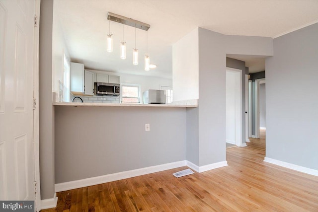 kitchen featuring appliances with stainless steel finishes, light hardwood / wood-style flooring, decorative light fixtures, kitchen peninsula, and white cabinets