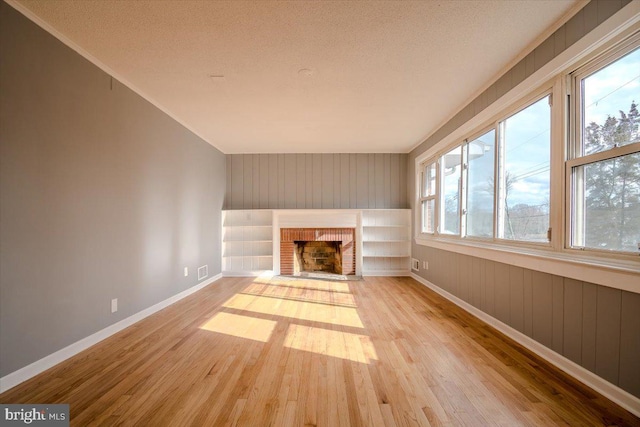 unfurnished living room featuring a brick fireplace, light hardwood / wood-style floors, and a textured ceiling