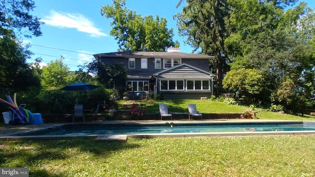 back of house with an outdoor pool, a lawn, and a chimney