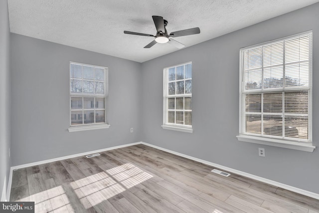 empty room with visible vents, a textured ceiling, baseboards, and wood finished floors