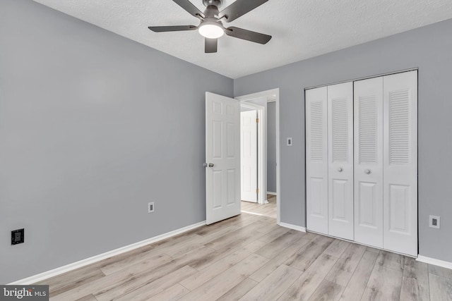 unfurnished bedroom featuring a textured ceiling, a closet, light wood-style flooring, and baseboards