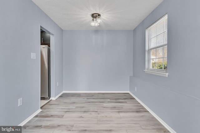 empty room with a textured ceiling, wood finished floors, and baseboards