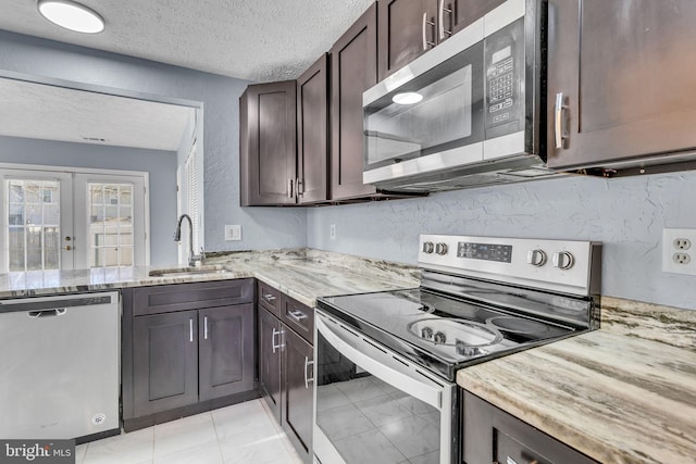 kitchen featuring light stone counters, stainless steel appliances, a sink, dark brown cabinetry, and a textured ceiling