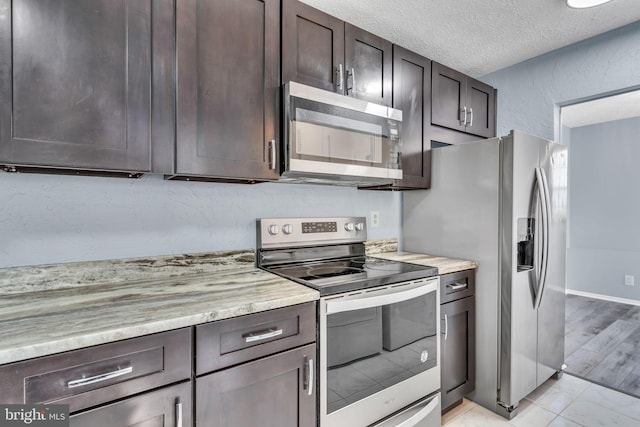 kitchen featuring a textured ceiling, stainless steel appliances, a textured wall, and dark brown cabinetry