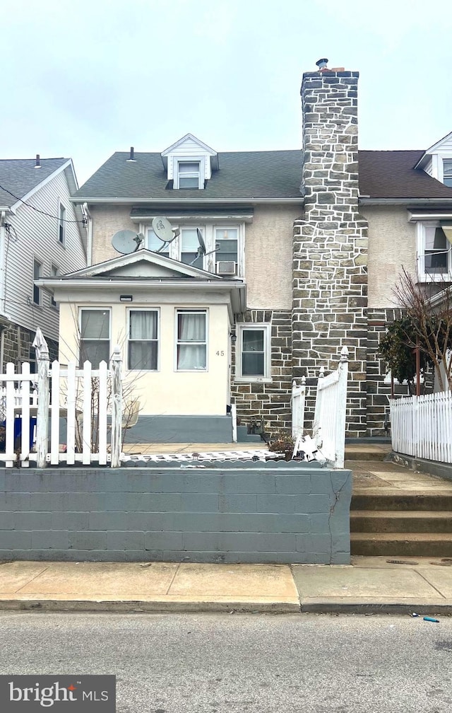 view of front facade with a fenced front yard, a chimney, and stucco siding