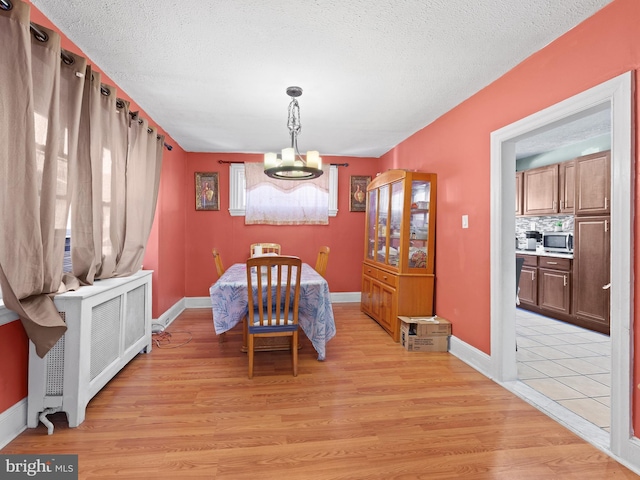 dining space featuring a textured ceiling, a notable chandelier, baseboards, light wood-type flooring, and radiator