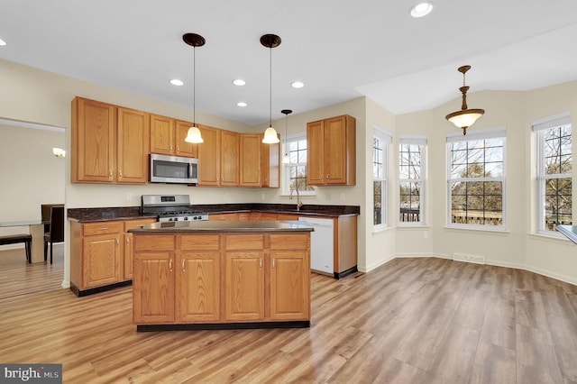 kitchen featuring stainless steel appliances, a sink, hanging light fixtures, light wood-type flooring, and dark countertops