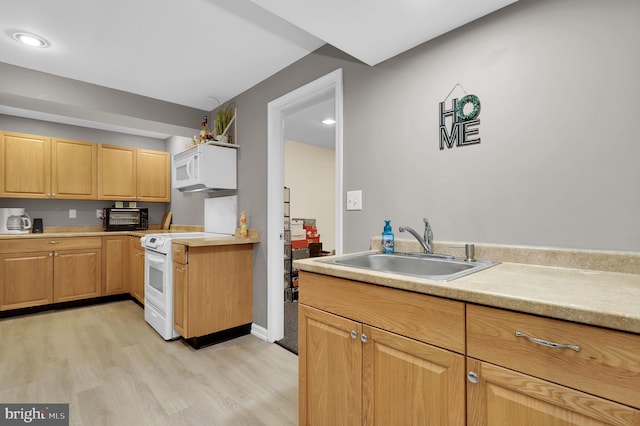 kitchen featuring white appliances, a sink, light countertops, light brown cabinetry, and light wood finished floors