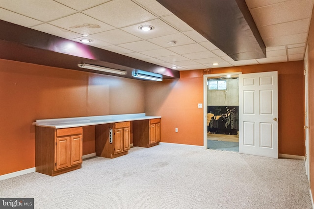 unfurnished office featuring baseboards, built in desk, a paneled ceiling, and light colored carpet