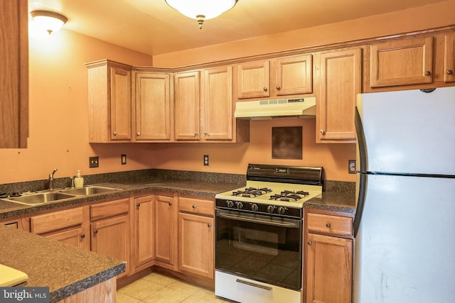 kitchen featuring under cabinet range hood, a sink, white gas range oven, freestanding refrigerator, and dark countertops