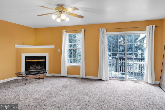 unfurnished living room featuring carpet floors, a glass covered fireplace, baseboards, and a ceiling fan