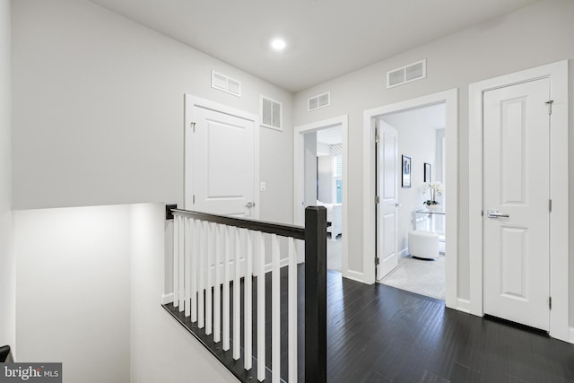 hall featuring dark wood-style flooring, visible vents, and an upstairs landing