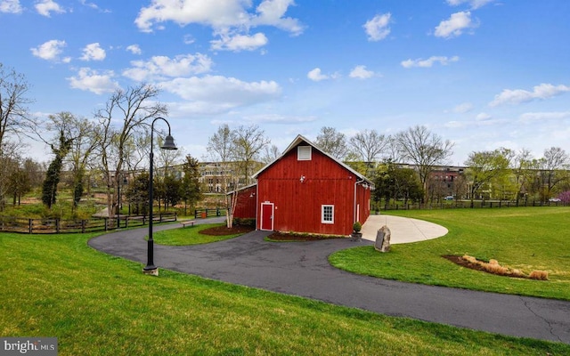 view of barn featuring driveway, fence, and a lawn