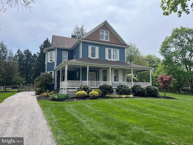 victorian house with a porch, a chimney, fence, and a front yard
