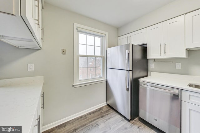 kitchen with appliances with stainless steel finishes, light hardwood / wood-style floors, light stone countertops, and white cabinets