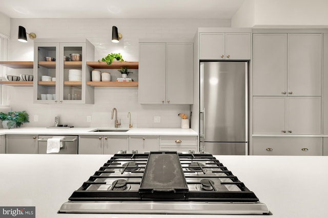 kitchen with light countertops, appliances with stainless steel finishes, open shelves, and a sink