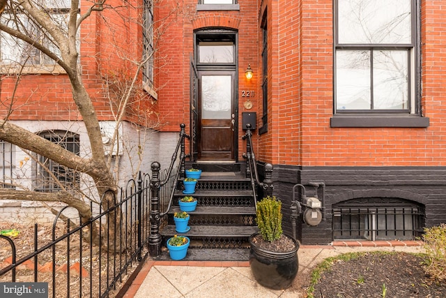 view of exterior entry featuring brick siding and fence