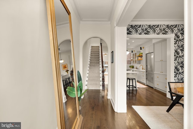 foyer featuring wallpapered walls, arched walkways, ornamental molding, dark wood-style flooring, and stairs