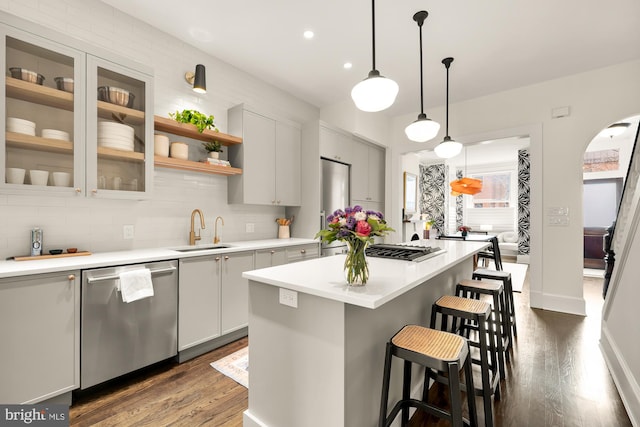 kitchen with stainless steel appliances, a sink, a kitchen island, light countertops, and decorative light fixtures