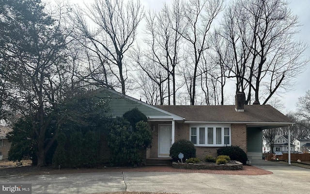 view of front of property with brick siding, a shingled roof, concrete driveway, a carport, and a chimney